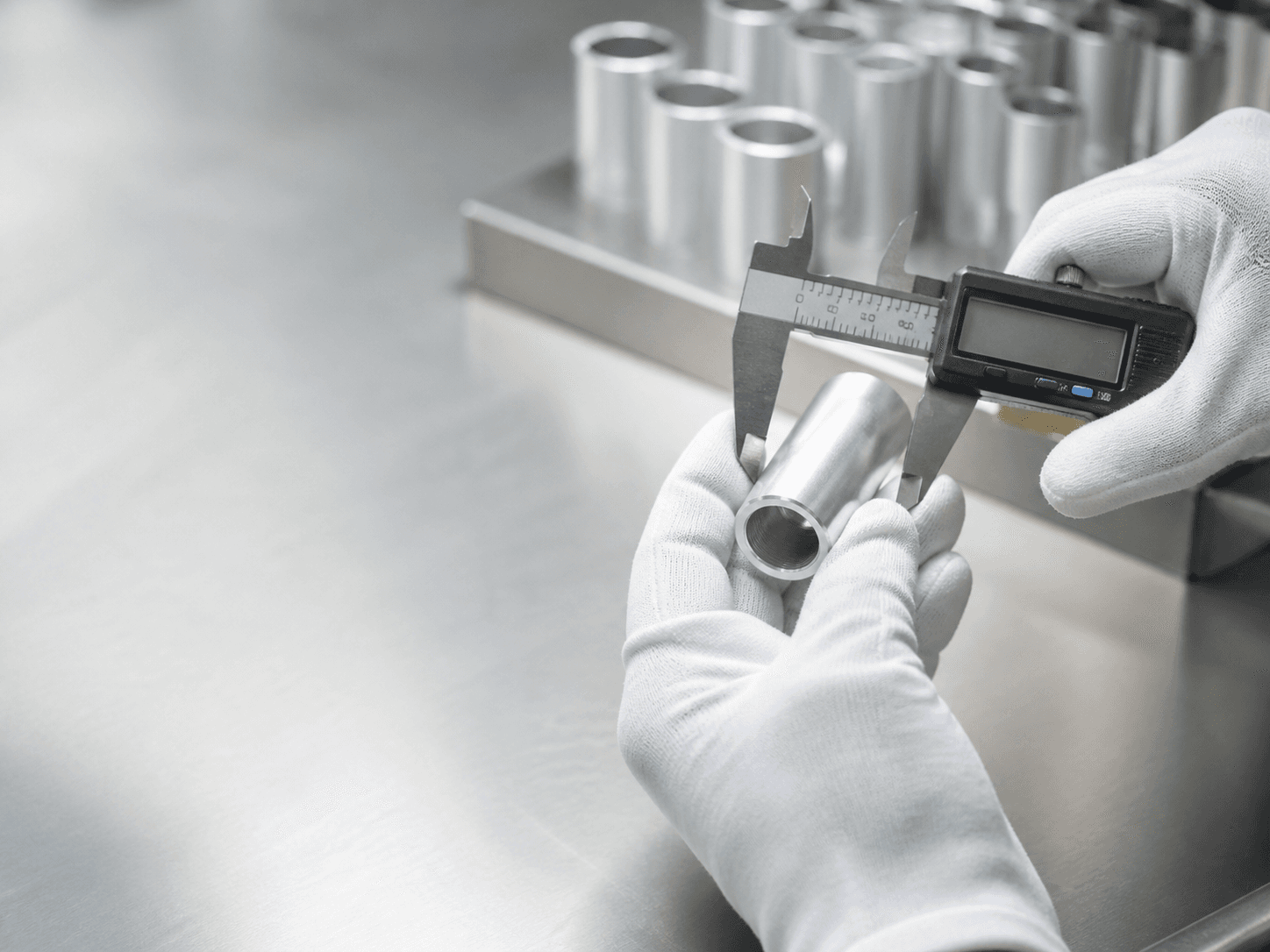 Quality technician measuring an aluminum atomizer component with a digital caliper